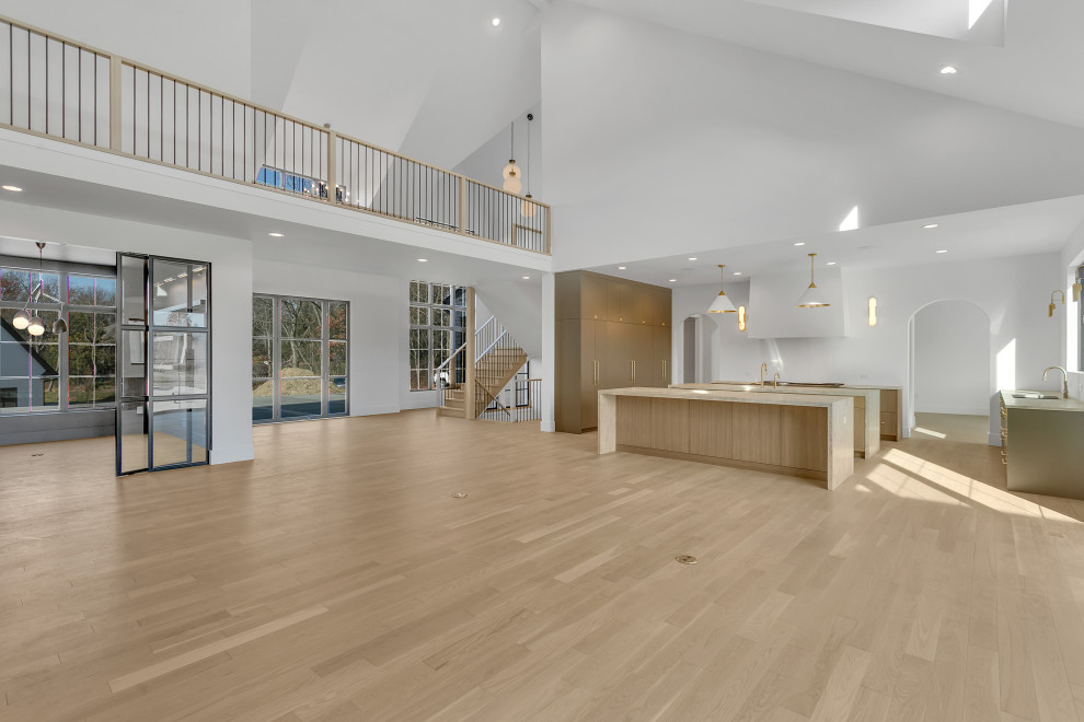 Example of a large transitional u-shaped light wood floor, beige floor and vaulted ceiling open concept kitchen design with an undermount sink, flat-panel cabinets, light wood cabinets, quartzite countertops, white backsplash, paneled appliances, two islands and beige countertops