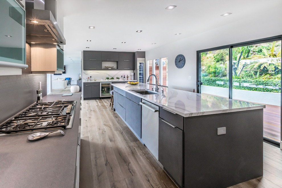 Large contemporary l-shaped open plan kitchen in Los Angeles with an undermount sink, flat-panel cabinets, grey cabinets, quartz benchtops, grey splashback, stone slab splashback, stainless steel appliances, dark hardwood floors, with island and brown floor.