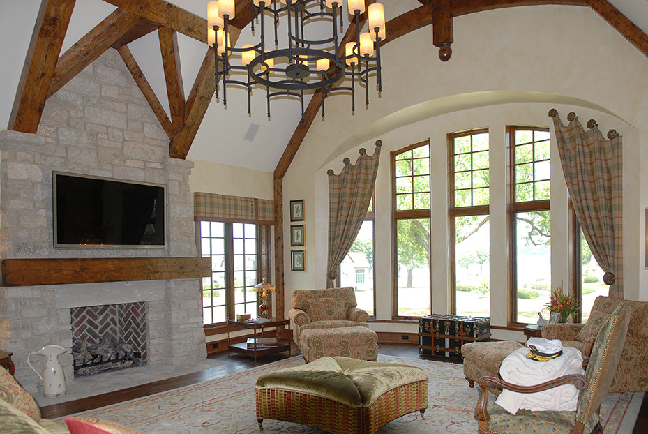 Large french country medium tone wood floor, brown floor and exposed beam living room photo in Chicago with a standard fireplace, a stone fireplace and a wall-mounted tv