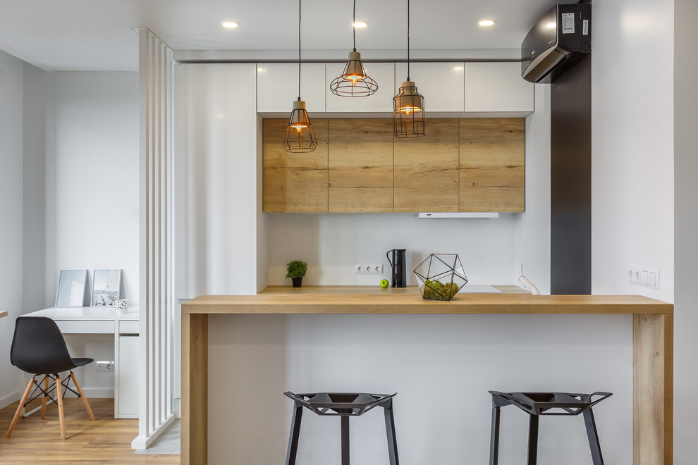 This is an example of a contemporary galley open plan kitchen in Moscow with flat-panel cabinets, white cabinets, wood benchtops, white splashback, a peninsula and brown benchtop.