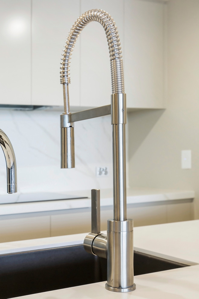 Photo of a mid-sized contemporary kitchen in Sydney with an undermount sink, flat-panel cabinets, beige cabinets, tile benchtops, multi-coloured splashback, porcelain splashback, stainless steel appliances, medium hardwood floors, a peninsula, brown floor and white benchtop.
