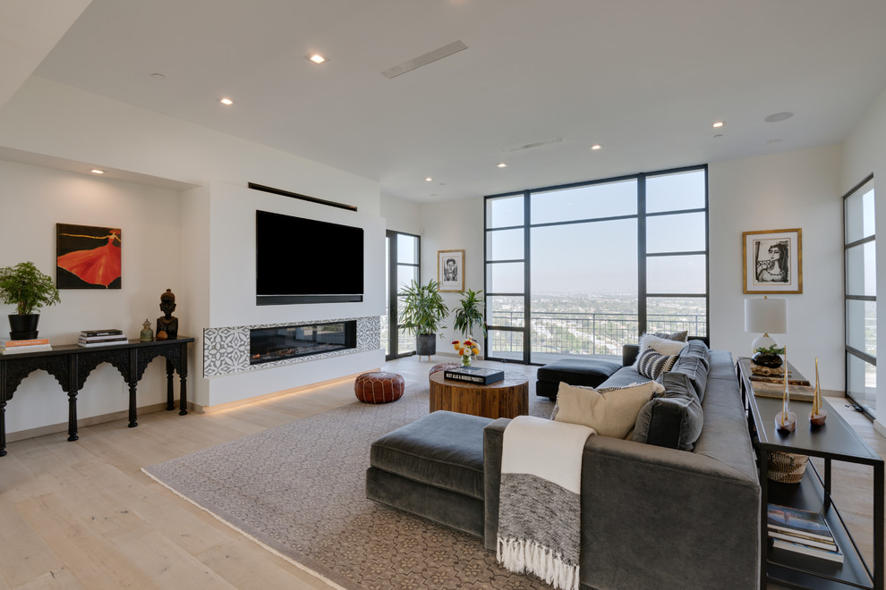 This is an example of a contemporary living room in Los Angeles with white walls, light hardwood floors, a ribbon fireplace, a tile fireplace surround, a built-in media wall and beige floor.