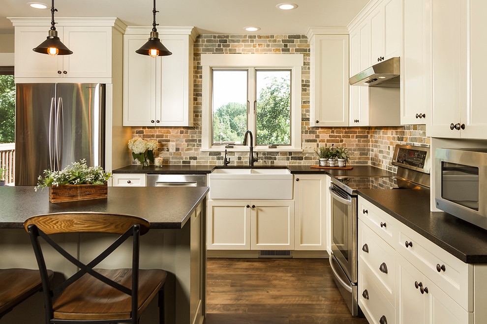 This is an example of a mid-sized country l-shaped eat-in kitchen in Minneapolis with a farmhouse sink, shaker cabinets, white cabinets, granite benchtops, blue splashback, stone tile splashback, stainless steel appliances, medium hardwood floors, with island, brown floor and black benchtop.