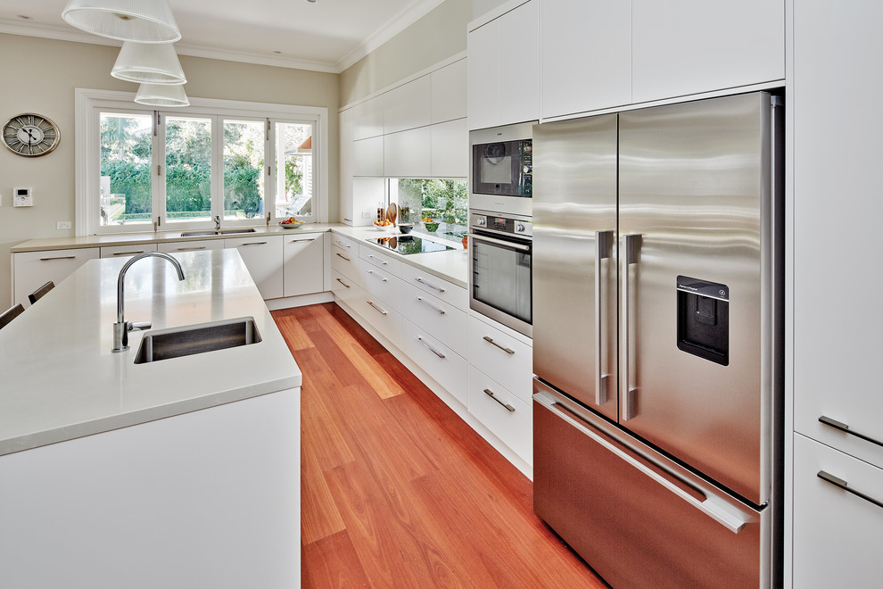 Design ideas for a large modern l-shaped kitchen pantry in Sydney with an integrated sink, flat-panel cabinets, white cabinets, quartz benchtops, window splashback, stainless steel appliances, medium hardwood floors, with island and brown floor.