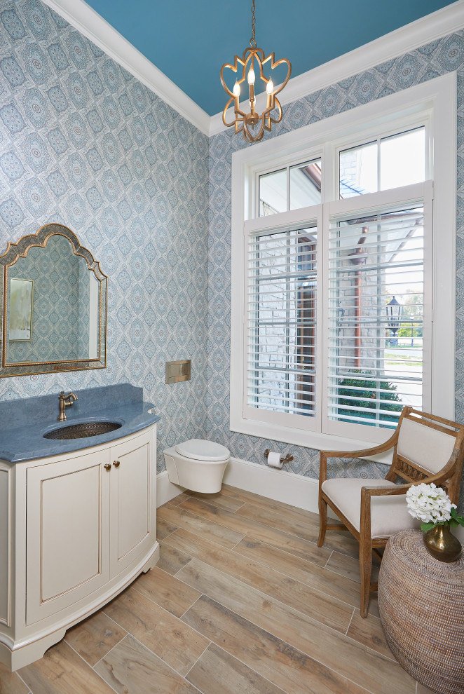 Cette photo montre une salle de bain beige et blanche avec des portes de placard blanches, WC suspendus, un mur bleu, parquet clair, un lavabo encastré, un sol beige, un plan de toilette bleu, meuble simple vasque, meuble-lavabo encastré et du papier peint.