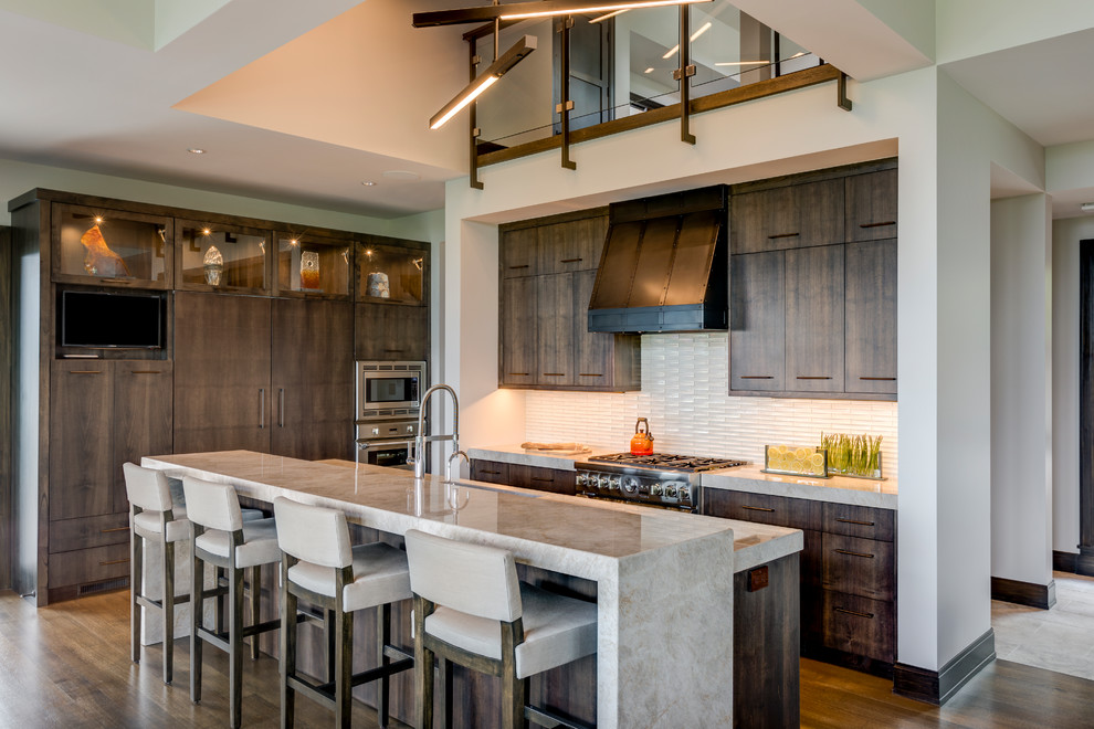 This is an example of a country u-shaped kitchen in Detroit with flat-panel cabinets, dark wood cabinets, white splashback, stainless steel appliances, dark hardwood floors, with island, brown floor and grey benchtop.