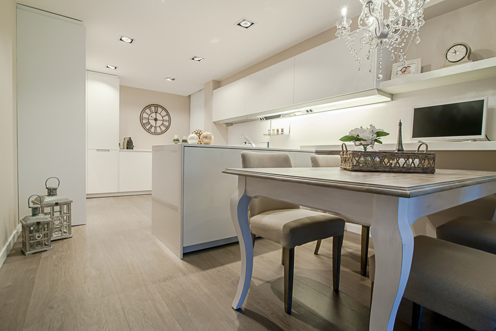 This is an example of a mid-sized transitional u-shaped open plan kitchen in Barcelona with flat-panel cabinets, white cabinets, white splashback, light hardwood floors and a peninsula.