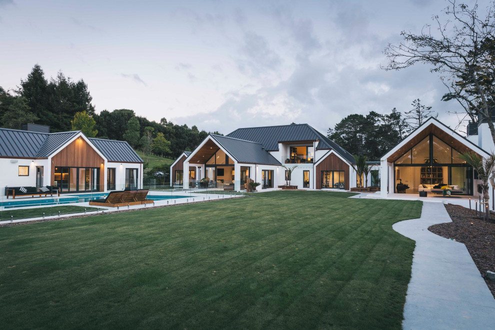 Inspiration pour une grande façade de maison blanche design en adobe à un étage avec un toit à deux pans, un toit en métal et un toit noir.
