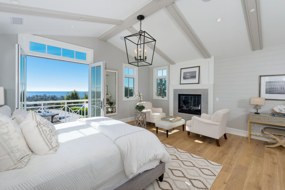 Design ideas for a large beach style master bedroom in Los Angeles with grey walls, medium hardwood floors, a standard fireplace, brown floor and a tile fireplace surround.