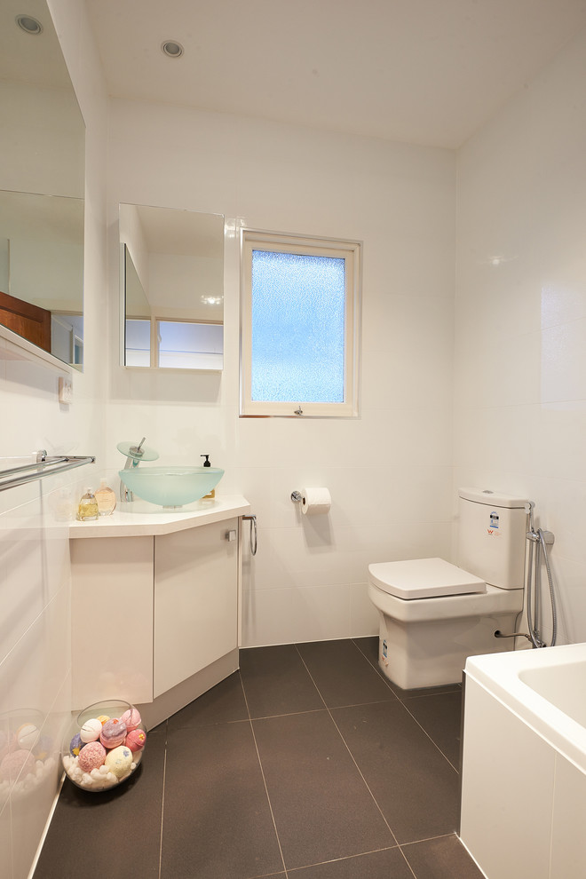 Inspiration for a small contemporary 3/4 bathroom in Melbourne with a console sink, flat-panel cabinets, white cabinets, engineered quartz benchtops, a drop-in tub, a shower/bathtub combo, a one-piece toilet, gray tile, ceramic tile, white walls and ceramic floors.