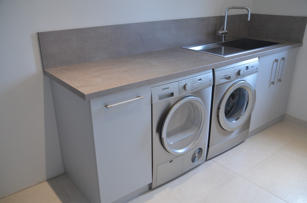 Photo of a large contemporary single-wall dedicated laundry room in Nice with an undermount sink, beaded inset cabinets, grey cabinets, laminate benchtops, grey walls, ceramic floors, a side-by-side washer and dryer, beige floor and grey benchtop.
