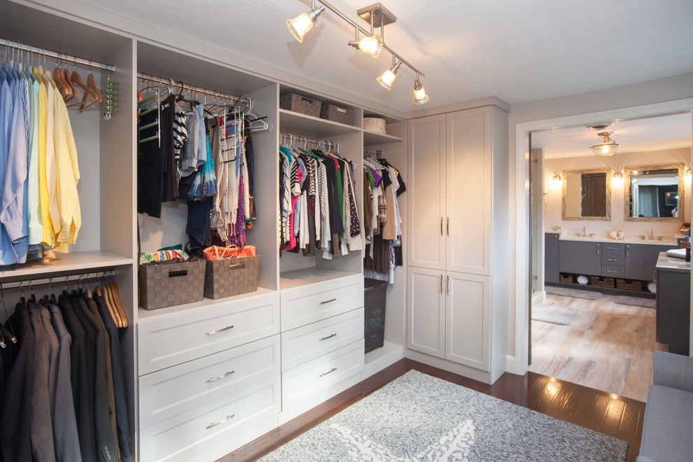 Large contemporary gender-neutral walk-in wardrobe in Boston with flat-panel cabinets, white cabinets and dark hardwood floors.