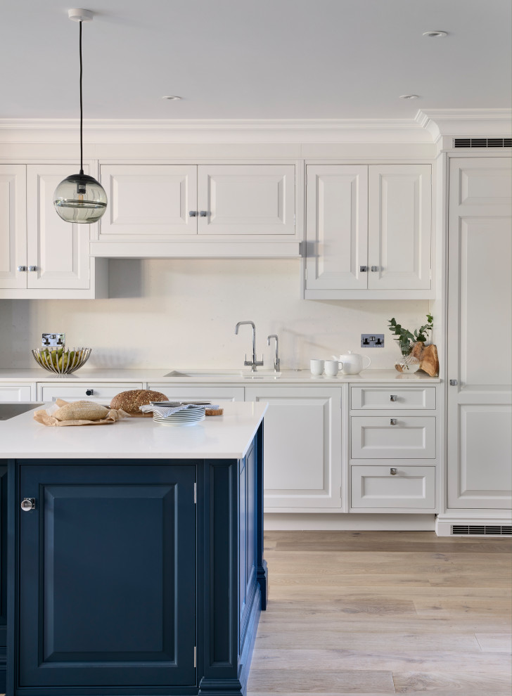 Offene, Große Klassische Küche mit integriertem Waschbecken, profilierten Schrankfronten, blauen Schränken, Quarzit-Arbeitsplatte, Küchenrückwand in Weiß, schwarzen Elektrogeräten, braunem Holzboden, Kücheninsel und weißer Arbeitsplatte in Buckinghamshire