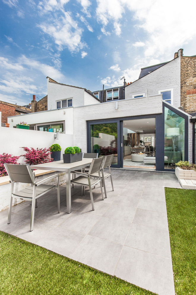 This is an example of a large contemporary backyard patio in London with natural stone pavers.