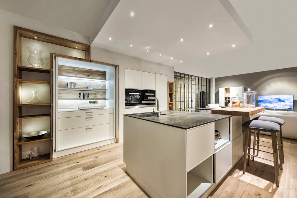 Offene, Einzeilige Moderne Küche mit Einbauwaschbecken, flächenbündigen Schrankfronten, weißen Schränken, hellem Holzboden, Kücheninsel und braunem Boden in Nürnberg