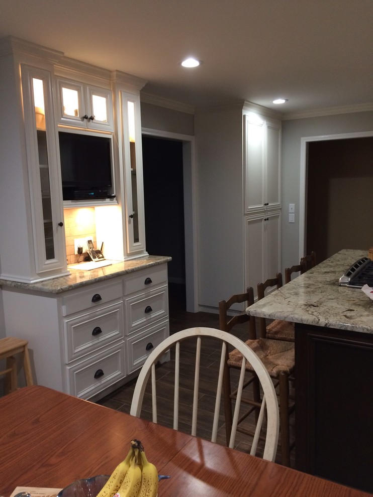 Inspiration for a large transitional l-shaped brown floor eat-in kitchen remodel in Birmingham with a farmhouse sink, recessed-panel cabinets, white cabinets, beige backsplash, stainless steel appliances and an island