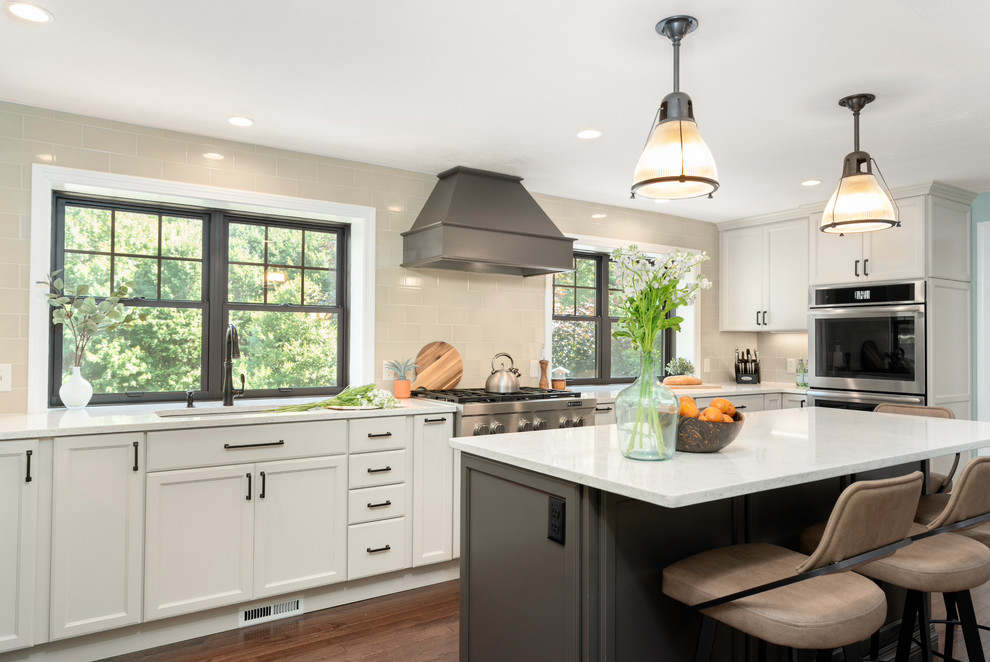 Country l-shaped kitchen in Boston with an undermount sink, recessed-panel cabinets, white cabinets, beige splashback, stainless steel appliances, dark hardwood floors, with island, brown floor and white benchtop.