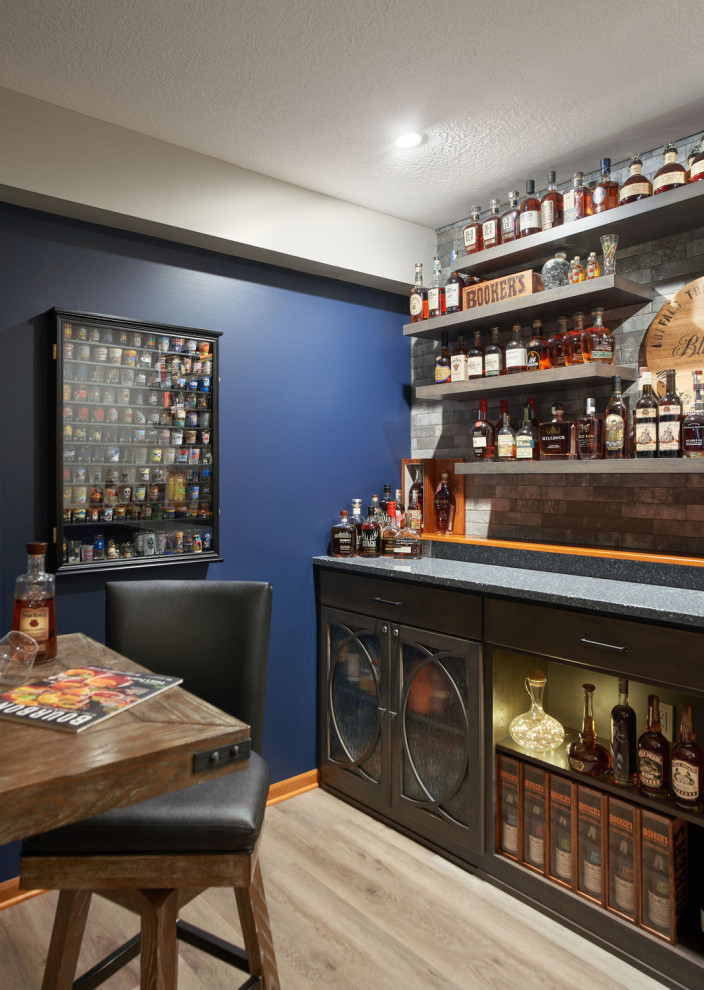 This is an example of a small traditional single-wall dry bar in Columbus with no sink, glass-front cabinets, medium wood cabinets, engineered stone countertops, multi-coloured splashback, brick splashback, vinyl flooring, grey floors and blue worktops.
