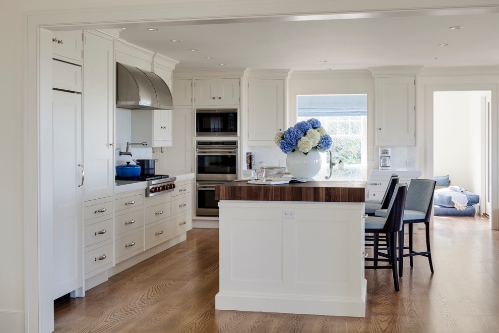 Inspiration for a large transitional l-shaped eat-in kitchen in Boston with an undermount sink, recessed-panel cabinets, white cabinets, marble benchtops, white splashback, stone slab splashback, stainless steel appliances, medium hardwood floors, with island and brown floor.