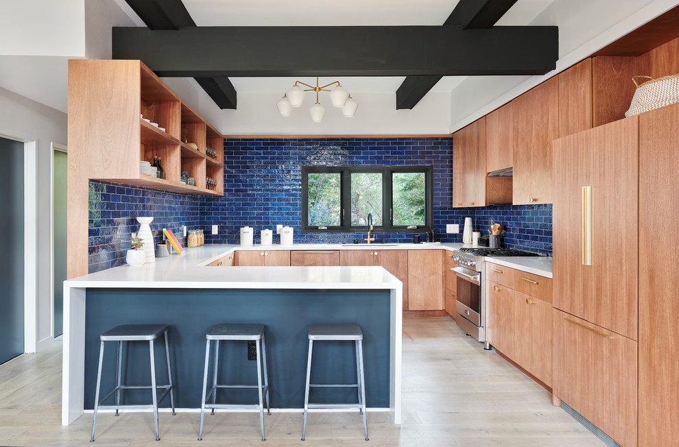 Photo of a midcentury u-shaped kitchen in San Francisco with an undermount sink, flat-panel cabinets, medium wood cabinets, blue splashback, stainless steel appliances, light hardwood floors, a peninsula, beige floor and white benchtop.