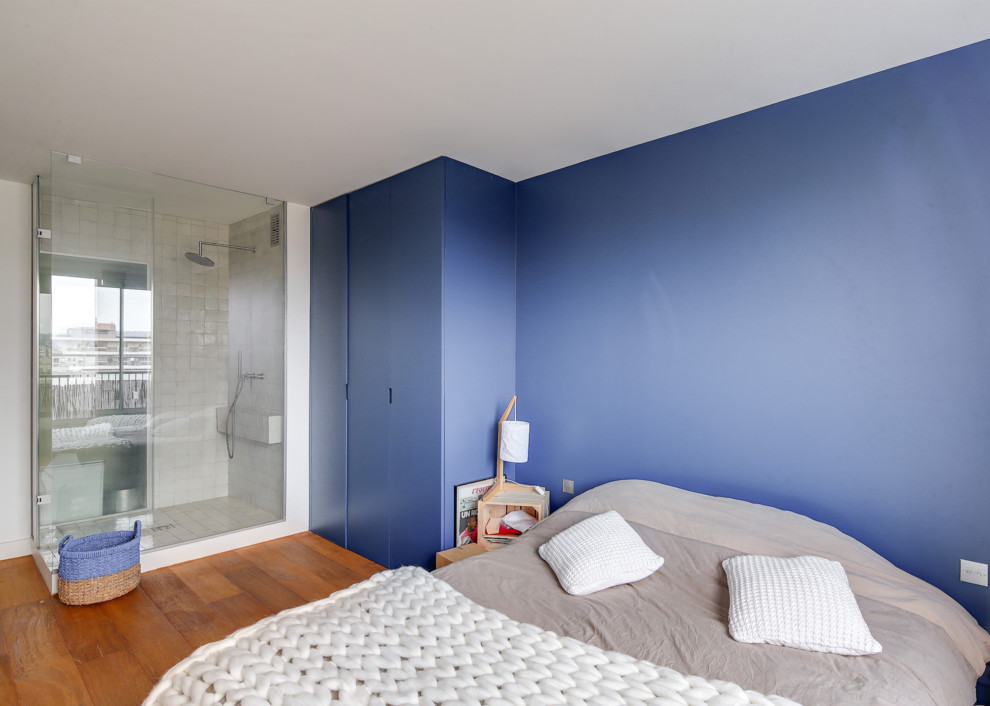Cette image montre une grande chambre parentale design avec un mur bleu, un sol en bois brun, aucune cheminée et un sol marron.