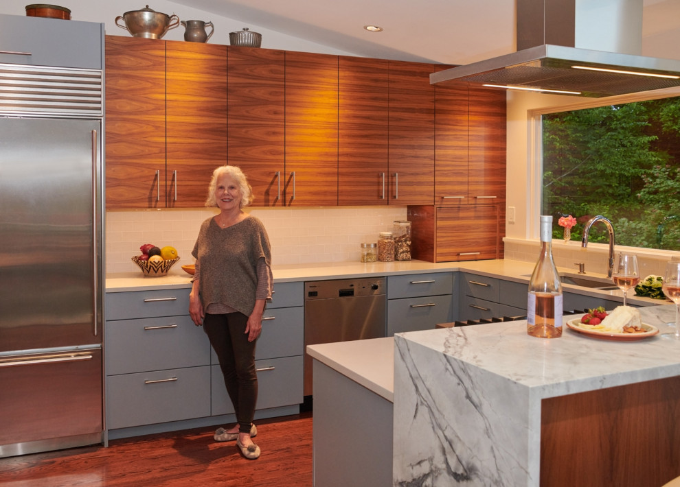 Mid-sized midcentury u-shaped eat-in kitchen in Seattle with an undermount sink, flat-panel cabinets, medium wood cabinets, solid surface benchtops, white splashback, ceramic splashback, stainless steel appliances, dark hardwood floors, a peninsula, brown floor, white benchtop and vaulted.