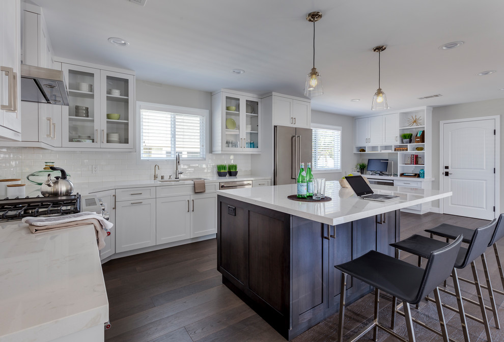 Mid-sized transitional l-shaped open plan kitchen in Los Angeles with an undermount sink, shaker cabinets, white cabinets, quartz benchtops, white splashback, subway tile splashback, stainless steel appliances, dark hardwood floors, with island and brown floor.