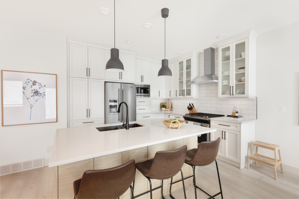 Photo of a small scandinavian l-shaped eat-in kitchen in Vancouver with an undermount sink, shaker cabinets, white cabinets, quartzite benchtops, white splashback, ceramic splashback, stainless steel appliances, vinyl floors, with island, multi-coloured floor and white benchtop.