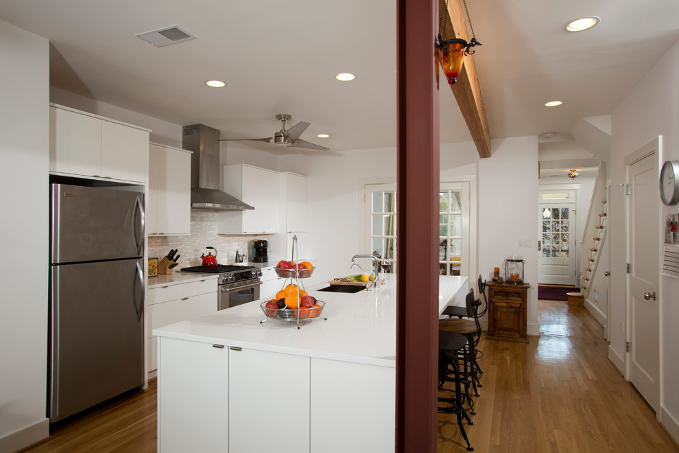 This is an example of a large contemporary single-wall eat-in kitchen in DC Metro with flat-panel cabinets, white cabinets, stainless steel appliances, an undermount sink, grey splashback, with island, solid surface benchtops, matchstick tile splashback and light hardwood floors.