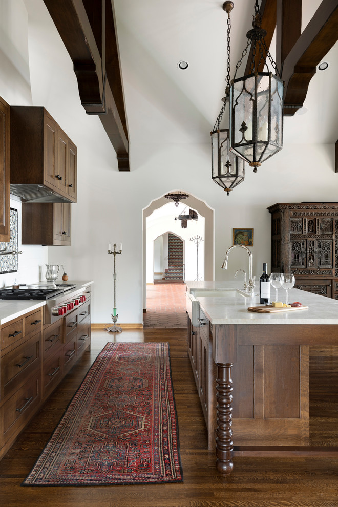 Large mediterranean galley kitchen in Minneapolis with a farmhouse sink, recessed-panel cabinets, dark wood cabinets, stainless steel appliances, dark hardwood floors, with island, brown floor, white benchtop, marble benchtops and white splashback.