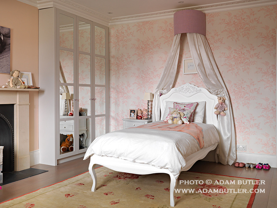 Photo of a mid-sized traditional kids' bedroom for kids 4-10 years old and girls in London with medium hardwood floors and pink walls.