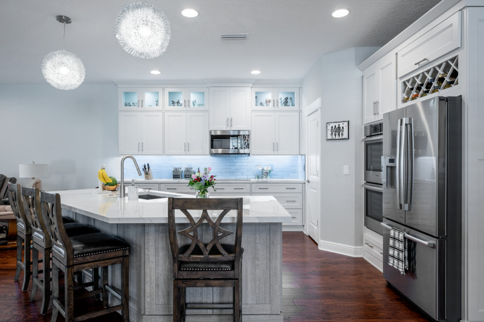This is an example of a mid-sized transitional l-shaped eat-in kitchen in Tampa with an undermount sink, shaker cabinets, white cabinets, tile benchtops, grey splashback, subway tile splashback, black appliances, medium hardwood floors, with island, brown floor and white benchtop.