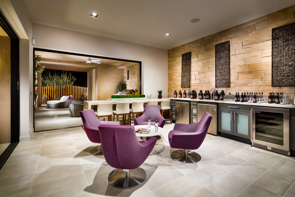 Inspiration for a large single-wall seated home bar in Phoenix with glass-front cabinets, grey cabinets, beige splashback, limestone splashback, porcelain floors, grey floor and white benchtop.