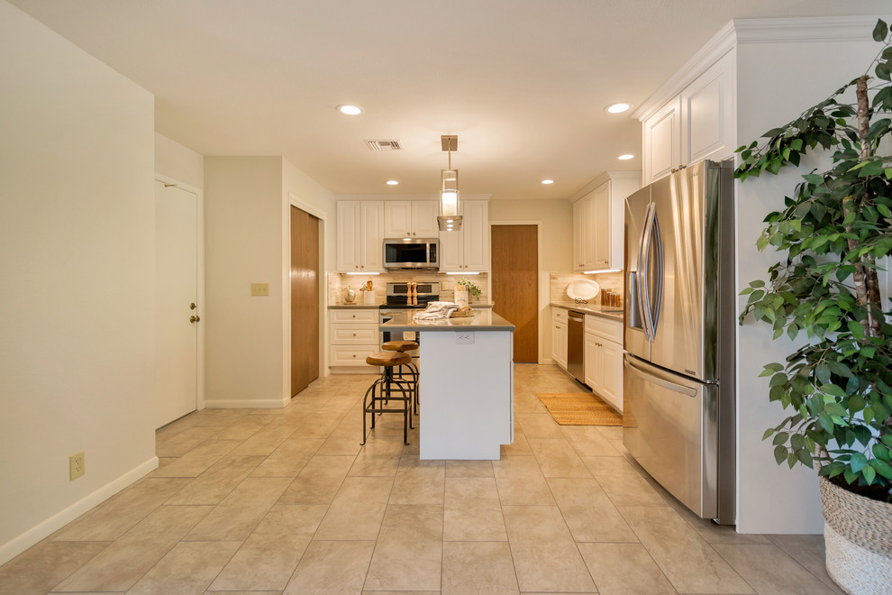 Inspiration for a large transitional l-shaped porcelain tile open concept kitchen remodel in Phoenix with an undermount sink, raised-panel cabinets, white cabinets, quartz countertops, beige backsplash, porcelain backsplash, stainless steel appliances and an island