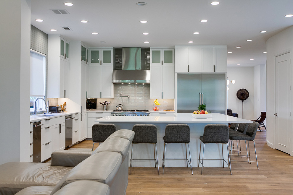 Photo of a large contemporary l-shaped open plan kitchen in Dallas with an undermount sink, shaker cabinets, white cabinets, quartzite benchtops, beige splashback, glass tile splashback, stainless steel appliances, light hardwood floors and with island.