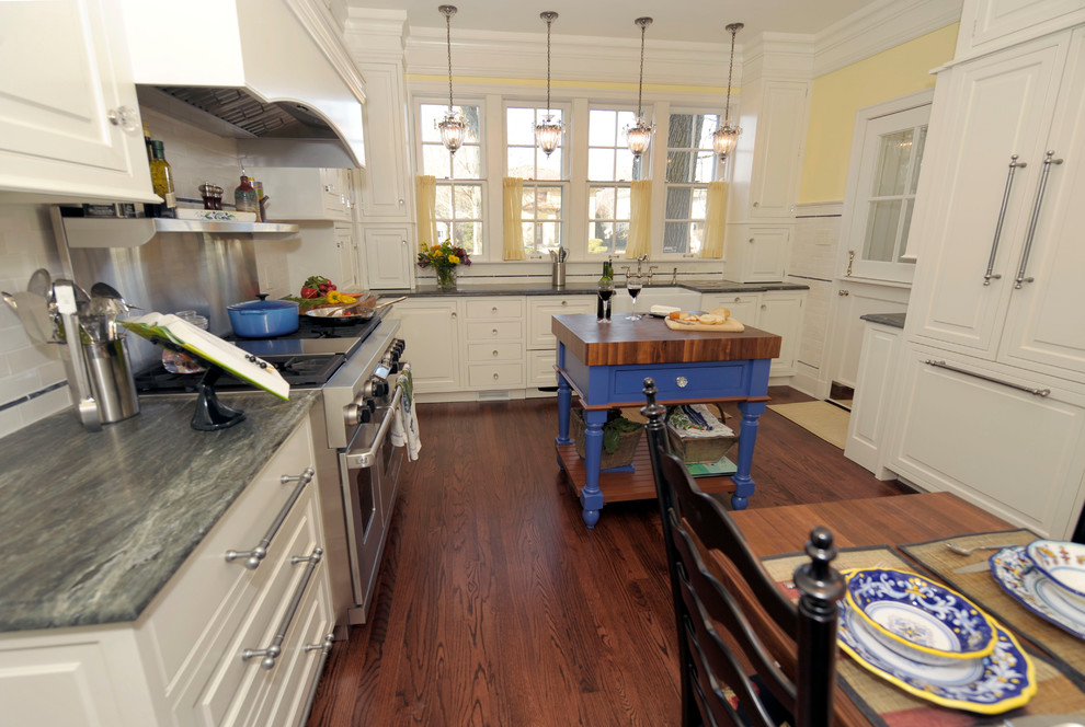 Mid-sized traditional galley separate kitchen in Chicago with a farmhouse sink, raised-panel cabinets, white cabinets, white splashback, subway tile splashback, stainless steel appliances, medium hardwood floors and with island.