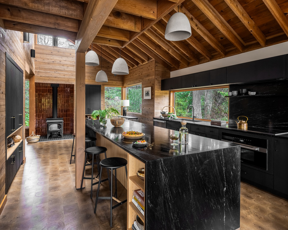 Example of a mountain style galley medium tone wood floor, brown floor, exposed beam, vaulted ceiling and wood ceiling kitchen design in Seattle with an undermount sink, flat-panel cabinets, black cabinets, window backsplash, black appliances, an island and black countertops