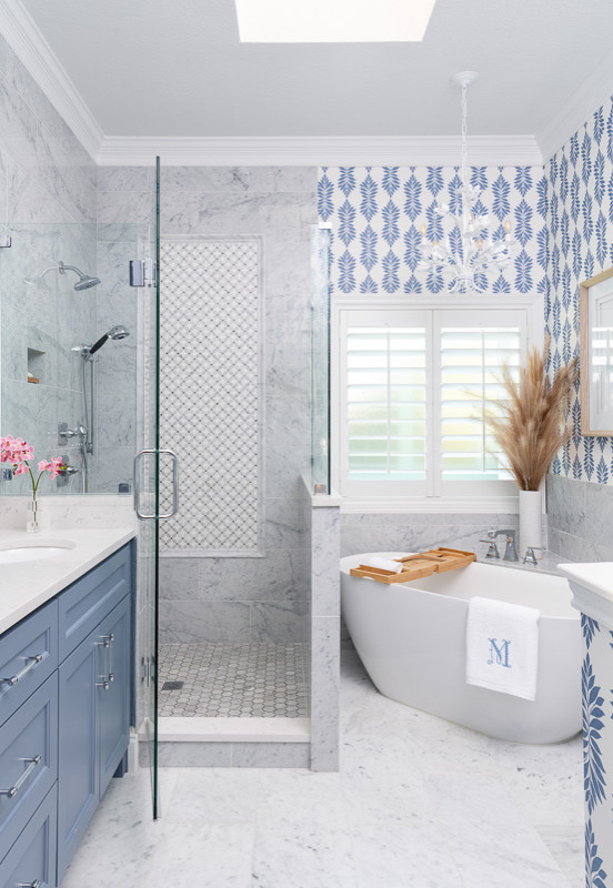 This is an example of a mid-sized transitional master bathroom in Dallas with blue cabinets, a freestanding tub, a corner shower, gray tile, multi-coloured walls, a drop-in sink, white floor, a hinged shower door, white benchtops, a single vanity, vaulted and wallpaper.