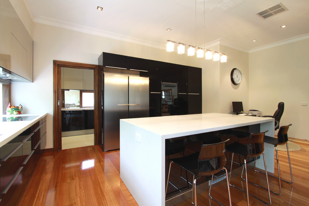 Photo of a mid-sized modern l-shaped open plan kitchen in Melbourne with an undermount sink, flat-panel cabinets, black cabinets, granite benchtops, glass sheet splashback, black appliances, medium hardwood floors and with island.