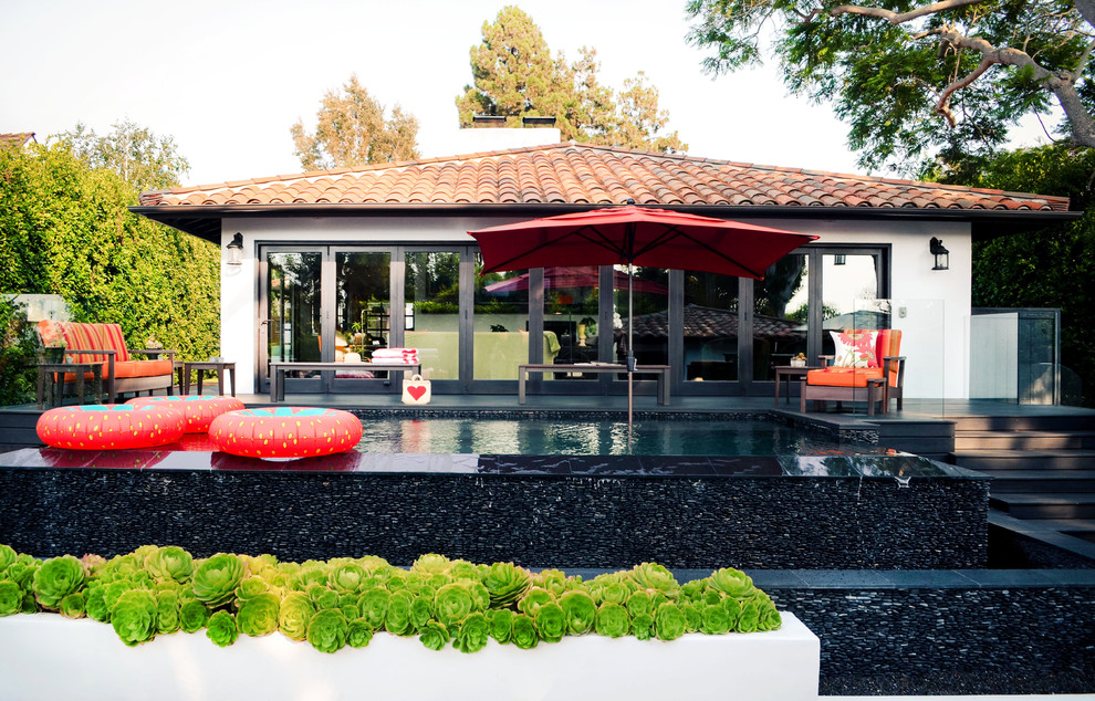 This is an example of a mid-sized mediterranean backyard rectangular infinity pool in Los Angeles with decking.