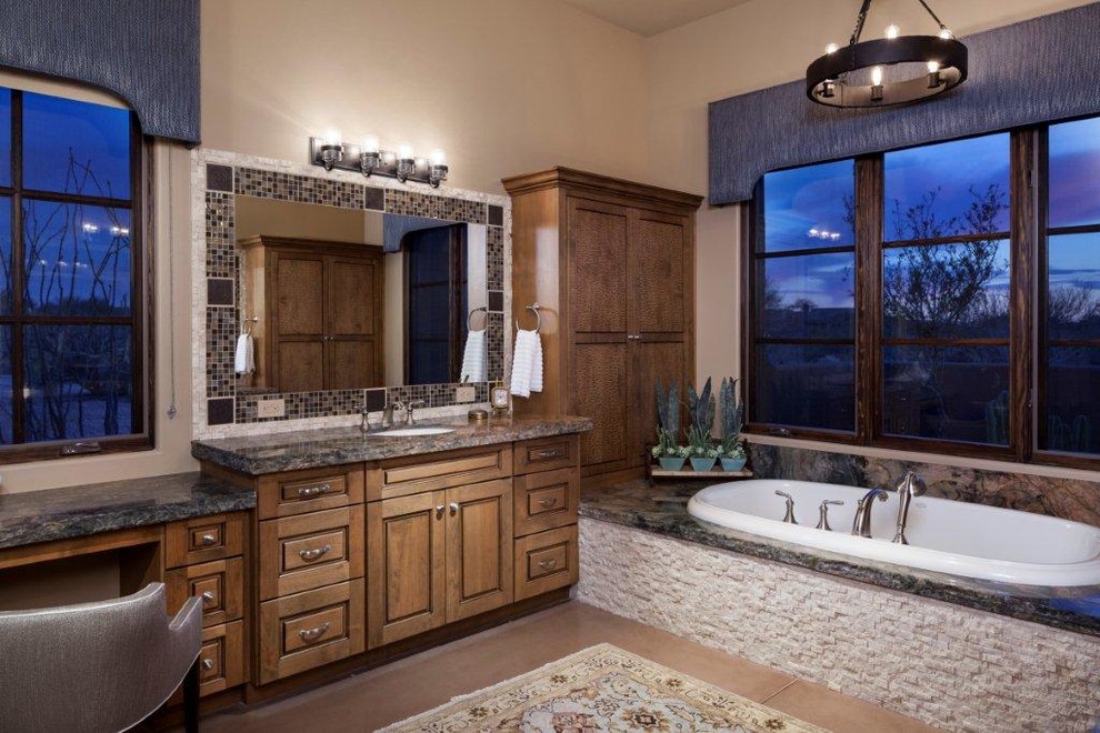 This is an example of a large master bathroom in Phoenix with raised-panel cabinets, medium wood cabinets, a drop-in tub, an open shower, a one-piece toilet, multi-coloured tile, beige walls, concrete floors, an undermount sink, granite benchtops, mosaic tile and beige floor.