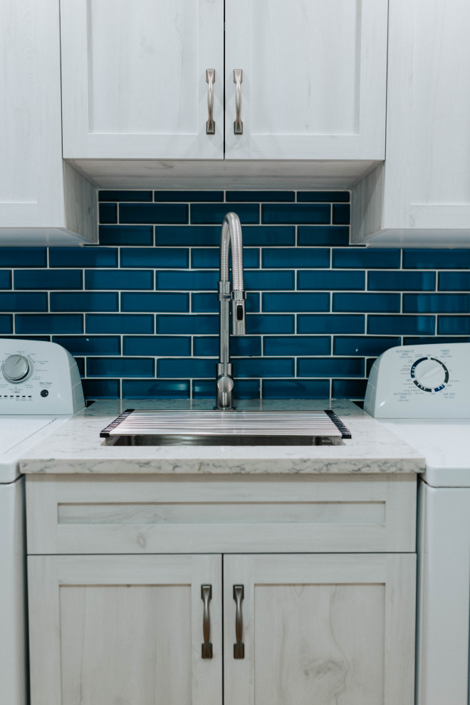 Photo of a mid-sized transitional utility room in Toronto with an undermount sink, shaker cabinets, grey cabinets, quartz benchtops, blue splashback, glass tile splashback, grey walls, medium hardwood floors, a side-by-side washer and dryer and grey benchtop.