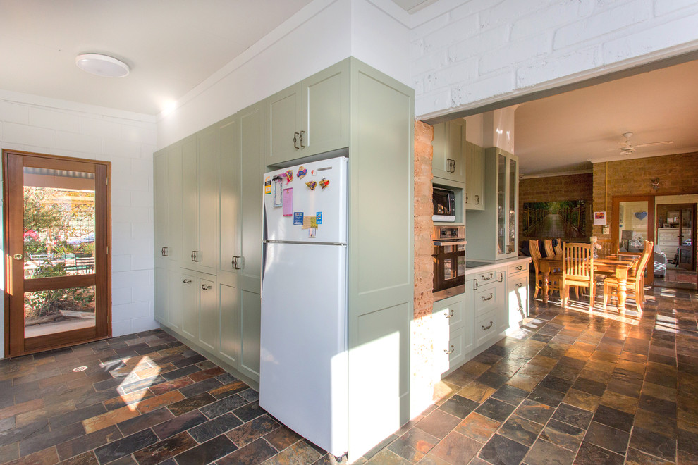 Small country galley kitchen in Other with a double-bowl sink, shaker cabinets, green cabinets, solid surface benchtops, white splashback, metal splashback, slate floors, multi-coloured floor and beige benchtop.
