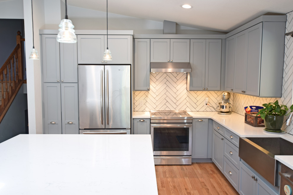 Example of a mid-sized transitional l-shaped vaulted ceiling open concept kitchen design in Denver with a farmhouse sink, shaker cabinets, gray cabinets, quartz countertops, white backsplash, stainless steel appliances, an island and white countertops