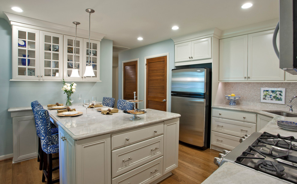 Inspiration for a mid-sized transitional l-shaped light wood floor and brown floor eat-in kitchen remodel in Baltimore with recessed-panel cabinets, white cabinets, marble countertops, a peninsula, an undermount sink, white backsplash, mosaic tile backsplash and stainless steel appliances