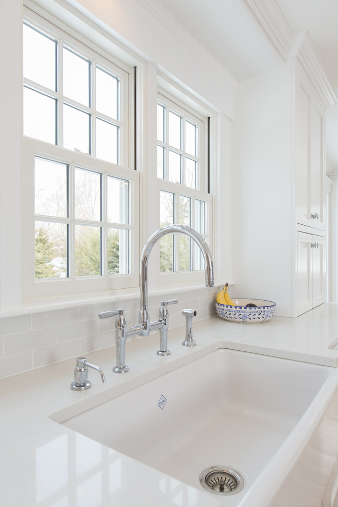 Open concept kitchen - mid-sized transitional l-shaped medium tone wood floor and brown floor open concept kitchen idea in Boston with a farmhouse sink, shaker cabinets, white cabinets, quartz countertops, white backsplash, subway tile backsplash, paneled appliances, an island and white countertops