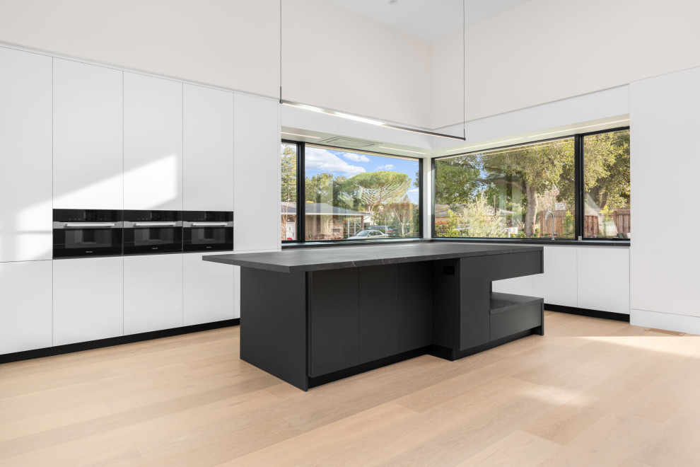Photo of a large modern galley open plan kitchen in San Francisco with an undermount sink, flat-panel cabinets, white cabinets, quartz benchtops, black appliances, with island and black benchtop.