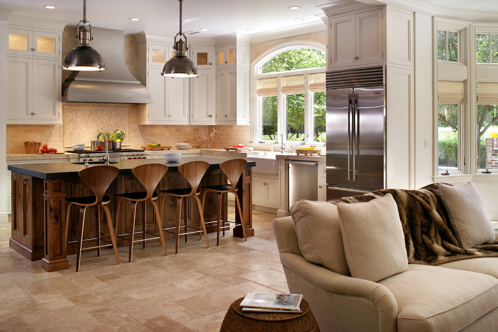 Large transitional l-shaped travertine floor and beige floor eat-in kitchen photo in New York with a farmhouse sink, recessed-panel cabinets, white cabinets, beige backsplash, stainless steel appliances, soapstone countertops, white walls and travertine backsplash