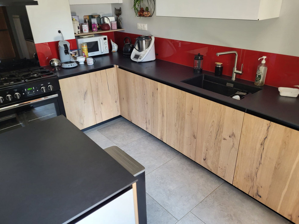 Cette photo montre une cuisine ouverte noire et bois tendance en L avec un évier 1 bac, un plan de travail en granite, une crédence rouge, un électroménager noir, îlot, un sol gris et plan de travail noir.