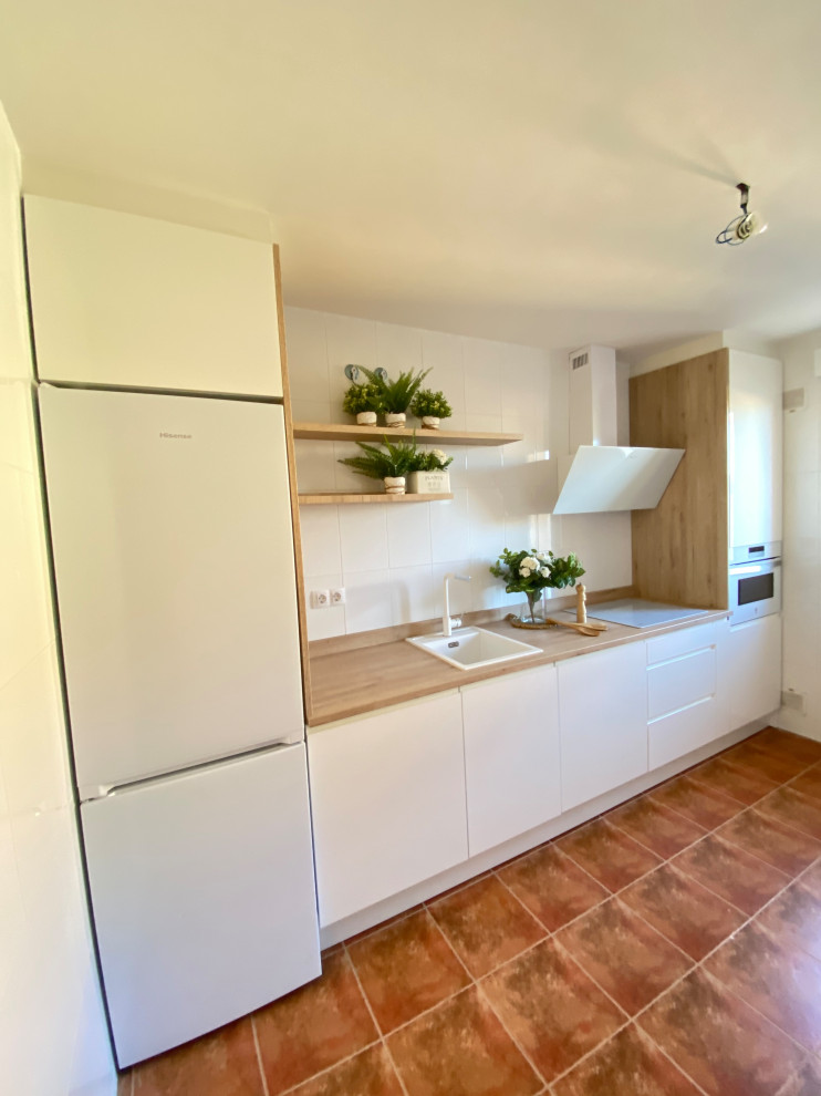 Photo of a mid-sized scandinavian single-wall separate kitchen in Other with a farmhouse sink, recessed-panel cabinets, white cabinets, wood benchtops, white splashback, engineered quartz splashback, white appliances, terra-cotta floors, multi-coloured floor and beige benchtop.